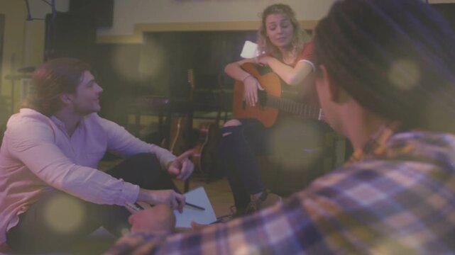 Left collaborator offering notebook, woman strumming guitar while partners marking song notes