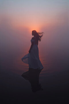 Silhouette of Woman in White Dress with Hair Blowing at Sunset Reflects