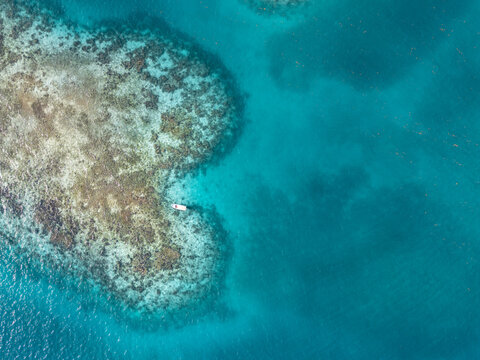 Aerial view of a small white boat anchored near a vibrant coral reef surrounded by crystal clear turquoise waters Guanaja, Bay Islands Department, Honduras.