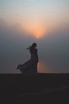 Silhouette of Woman in Flowing Dress at Sunset by the Water's Edge