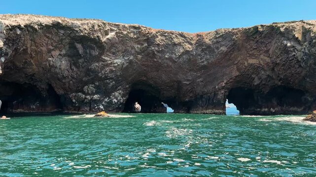 Cinematic wide shot of massive coastal island cliff with natural sea caves and erosion tunnels beneath solid rock formation near Paracas National Reserve, Peru