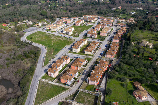 High-angle aerial view of a planned workers' housing neighborhood in Corfu, Greece, revealing the street layout and architecture among green fields.