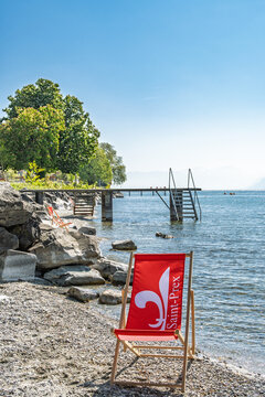 Chaise longue rouge avec blason de Saint-Prex sur une plage de galets au bord du lac L&eacute;man, Suisse