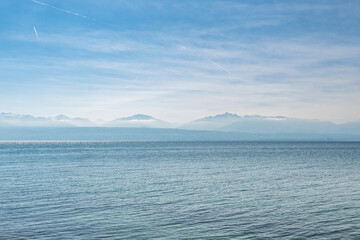 Fototapeta premium Vue panoramique sur le lac Léman et les Alpes françaises depuis Saint-Prex sous un ciel voilé, Suisse