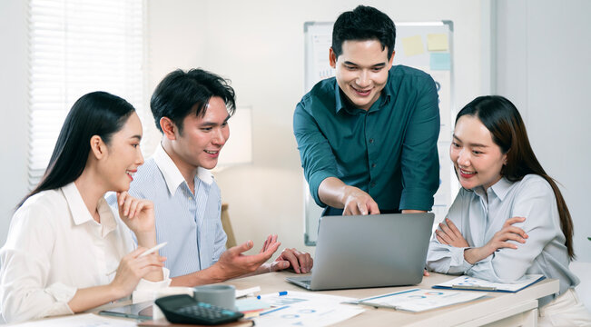 Diverse Asian business people collaborating and smiling at laptop in modern office.