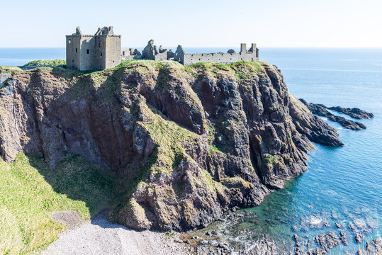 Dunnottar Castle near Stonehaven in Scotland, UK: Medieval cliff‑top fortress in ruins rising above a rocky coast, with blue sea, rugged landscape and dramatic coastal scenery.