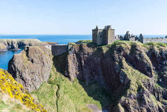 Dunnottar Castle near Stonehaven in Scotland, UK: Ruined medieval fortress perched on a steep coastal cliff above the sea, surrounded by rugged landscape and dramatic views under a clear blue sky