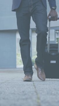 Vertical video: Businessman walking toward camera pulling suitcase holding phone heading meeting