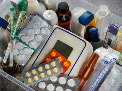 Medicines, blood pressure monitor, thermometer, syringes, inhaler, tablets in blisters, and other first aid items are neatly placed in a plastic box. First aid kit for home, clinic, business.