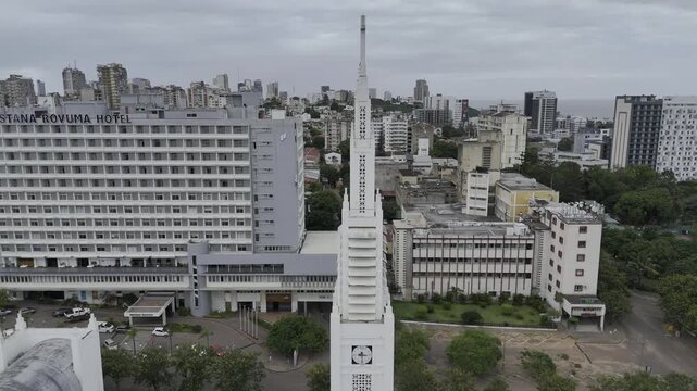 Drone orbits right from side to front of white cathedral clock tower and steeple on an overcast day in Maputo, Mozambique