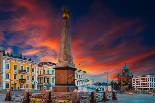 The Stone of the Empress (Keisarinnankivi) obelisk monument standing prominently in Market Square with historic buildings and the Uspenski Cathedral under a stunning sunset sky