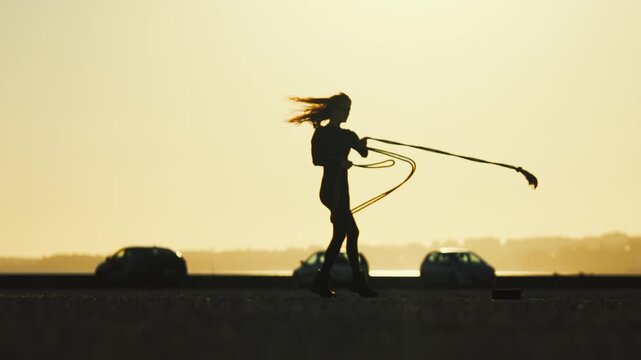 Woman pulls rope at sunset on a highway while cars pass by in the background