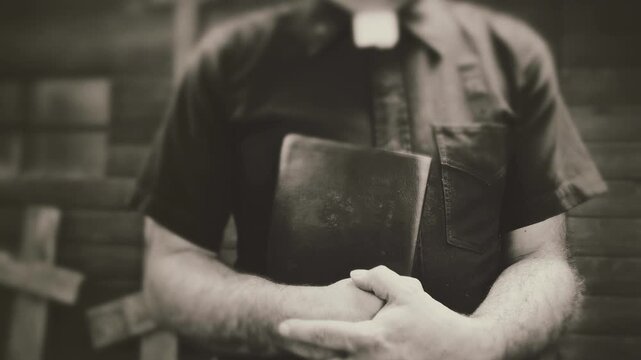 Clergyman, reverend or priest wearing a clerical collar and clutching a bible. Preacher preaching the gospel in front of an old rustic rural church or cemetery.
