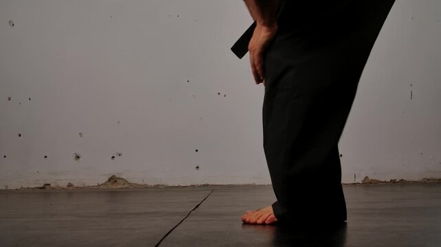 Close up of the legs of a man practicing Wing Chun in a black kimono, demonstrating his skills against a gray studio backdrop, showing self defense training and martial arts techniques.