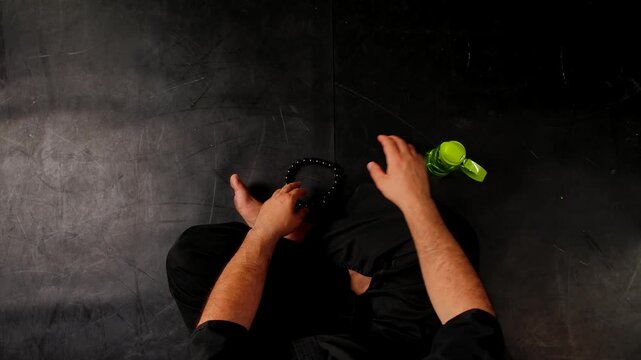 Top view of a martial arts master in a traditional black kimono sitting in the lotus position and meditating before training, fingering prayer beads.
