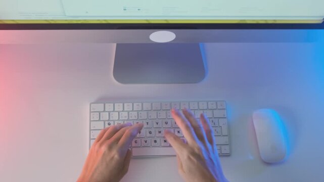 Overhead view of woman typing on desktop keyboard with mouse, stylish workspace with blue and pink lighting, creative digital workflow, modern office setup and online work concept