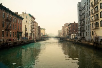 Naklejka premium Urban canal lined with historic buildings and fire escapes under a hazy sky