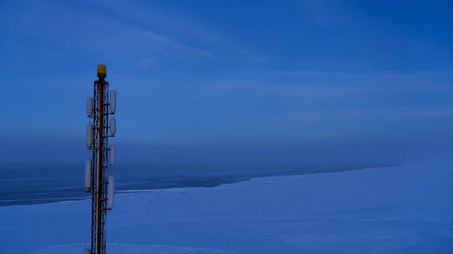 A telecommunications tower illuminated against a twilight sky, surrounded by vast snowfields and a sense of isolation