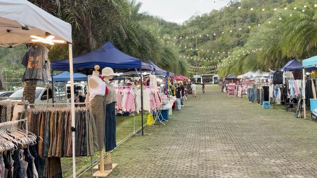 Evening flea market scene with clothing stalls and mountain backdrop in Thailand.
