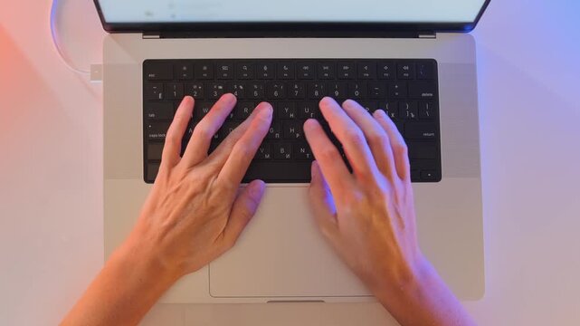 Top view of female hands typing on laptop keyboard at desk, working on computer with soft colored lighting, remote work, online communication and digital productivity in modern workspace