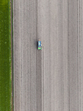 Aerial view of a tractor working on a large ploughed field with straight parallel furrows and a green grass border in Midden.