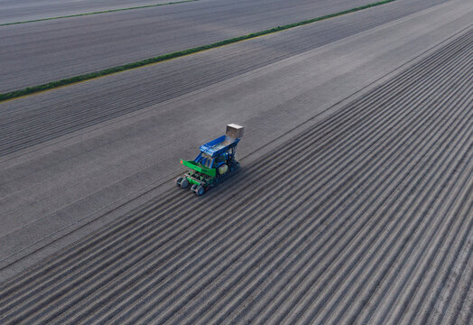 Aerial view of a blue and green agricultural planter machine working on a large field with perfectly aligned soil furrows.