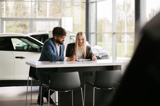 Car salesman assisting woman signing purchase contract