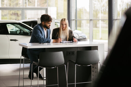 Car salesperson assisting woman with purchase contract