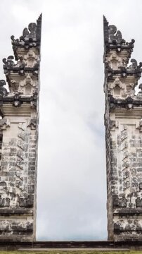 Ancient gateway formed by two stone towers with detailed reliefs frames an open arch, weathered texture, and expansive sky, conveying historical significance and architectural craftsmanship