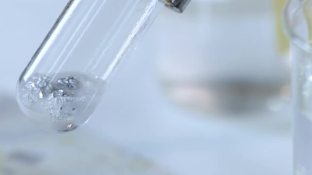 Chemical reaction in glass test tube with bubbling silver liquid and metal pieces in laboratory environment.