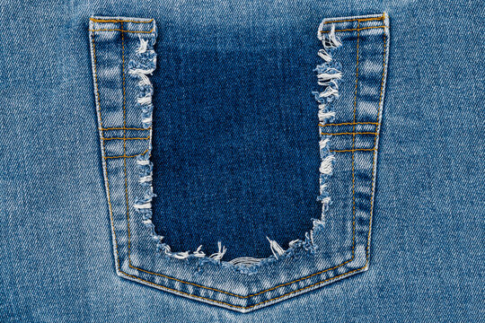 Ripped denim fabric showing a pocket area with frayed edges in a casual style