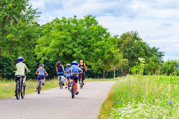 Obraz premium Group of people riding bicycles on a path surrounded by trees and green grass on a sunny day in summer