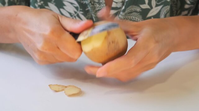 woman peeling potato front view removing skin with knife in hands, preparing vegetable for cooking meal, home kitchen routine, fresh ingredient processing and daily food prep activity