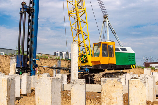 Crawler-mounted pile driving rig with yellow lattice boom and blue hydraulic hammer installing concrete piles in excavation pit