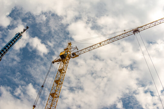 Low angle view of yellow tower crane showing lattice structure jib with trolley and steel cables against dramatic cloudy sky
