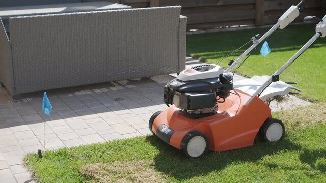 A man uses a professional gasoline scarifier to remove moss and thatch from a green lawn in a private house backyard.