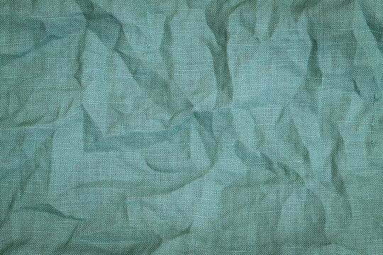 Texture of wrinkled fabric in light blue color spread on a flat surface during daylight hours