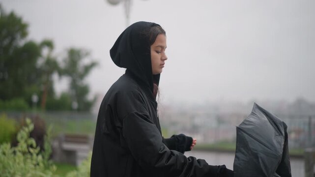 Female faces storm with umbrella and resolve. Woman withstands wind rain and broken umbrella in city. Determined woman on city overlook handling storm with makeshift canopy and resilience