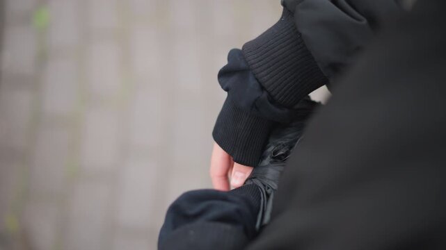 Woman adjusting glove on wet sidewalk, closeup of hand in fingerless glove and black coat, rainslick cobblestones and subtle droplets, introspective commuter fumbling umbrella strap while waiting