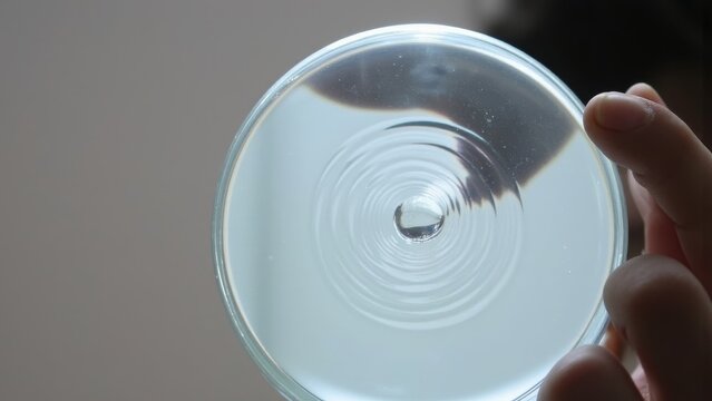 Hands holding a transparent glass with concentric circular ridges, spinning it slowly.