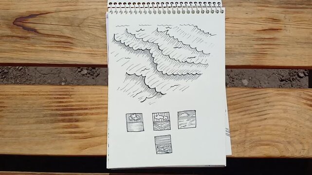 A sketch of sea waves has been drawn. The drawing is drawn in a sketchbook and lies on a bench, and the wind is turning the pages of the sketchbook.