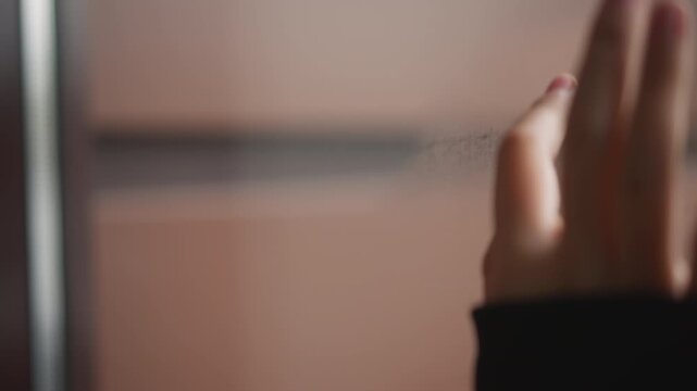 Closeup of hand and breath in cozy moment. Child playfully interacts with fogged window in indoor warmth. Tender scene of child tracing tiny shapes on fogged glass with warm breath