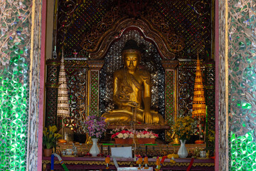 Fototapeta premium Golden Buddha statue sitting in a sacred shrine surrounded by elaborate colorful glass mosaic walls.