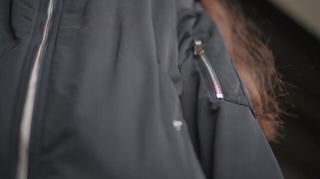 Closeup black jacket pocket zipper, rainy street commute, woman tucks hand into pocket near puddle, textured nylon fabric, subtle raindrops on sleeve, muted city tones and reflective pavement