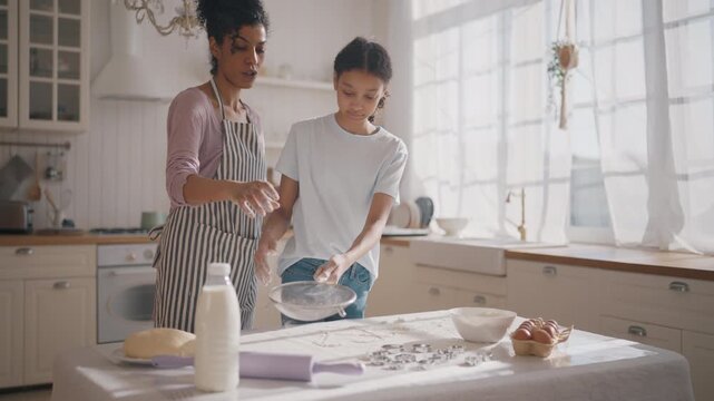 Calm sunny sunday morning at home, mom and daughter cooking dough for cookies. African american woman and her teenage daughter sifting flour for pizza or pie, make homemade bakery for family dinner