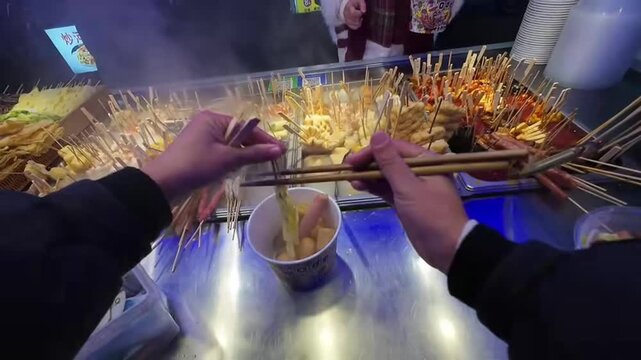 Guangzhou, Guangdong - May 1 2026: Various traditional meat and vegetable skewers steaming in hot broth at a busy night market stall in China.