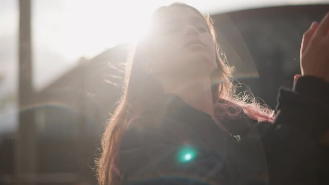 Young woman dancing in sunlit rain with expressive gestures, dancer enjoying blissful release as droplets catch rim light, playful hair toss and rhythmic sway near urban rail, cinematic flare