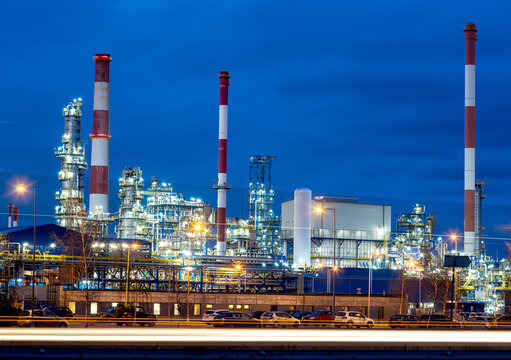 Petrochemical refinery at blue hour with industrial lights and chimneys.