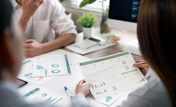 Businesswoman holding and analyzing financial chart during a team meeting.