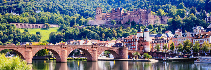 Naklejka premium Castle stands on hill near river in Heidelberg, Germany during sunny day with clear sky and green trees in the background